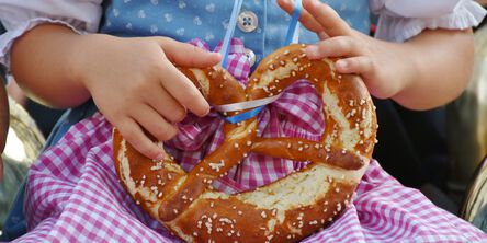 Person im Dirndl hält eine Brezel im Schoß